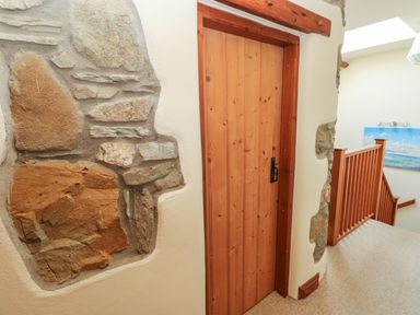 A wooden door set in a wall with exposed stone details next to a hallway with wooden railing and carpeted floor at 2 Yr Hen Felin Castle Morris near Letterston