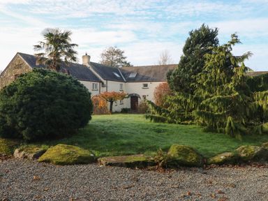 A house with a stone and plaster exterior surrounded by various trees and bushes at 2 Yr Hen Felin Castle Morris near Letterston