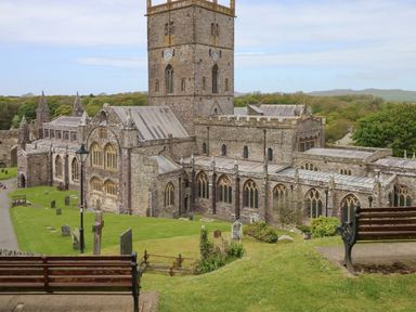 A stone church with a tall clock tower surrounded by grass and gravestones with benches in the foreground at 2 Yr Hen Felin Castle Morris near Letterston