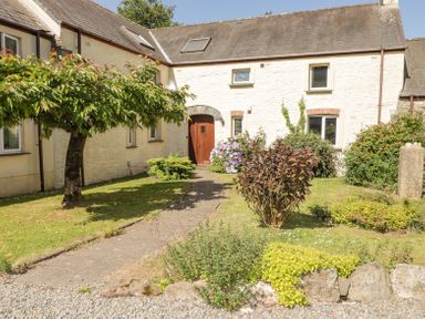 A stone cottage with a wooden door and garden with trees and shrubs at 2 Yr Hen Felin Castle Morris near Letterston