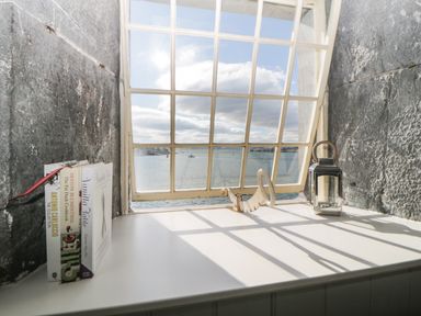 A white window sill with books on the left and a lantern on the right with a view of water through a grid window at Clarence Riverside Royal William Yard Plymouth