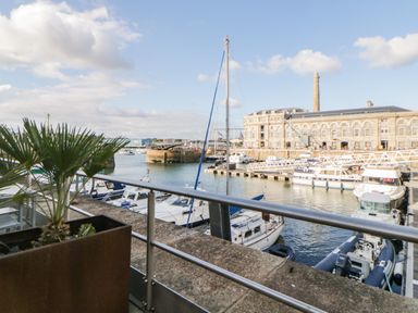 A marina with boats docked near a historic building with a chimney and a potted plant on a balcony at Clarence Riverside Royal William Yard in Plymouth