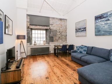 A living room with a blue sofa a wooden floor a television and a dining table at Clarence Riverside Royal William Yard Plymouth