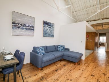 A living room with a blue sectional sofa and two paintings on the wall at Clarence Riverside Royal William Yard in Plymouth