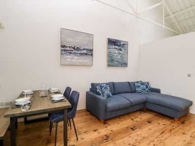 A living room with a blue sectional sofa and a wooden dining table with four place settings at Clarence Riverside Royal William Yard Plymouth