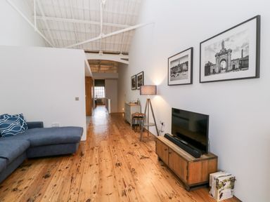 A living room with a blue sectional sofa a wooden TV stand with a television and black and white photos on the wall at Clarence Riverside Royal William Yard in Plymouth