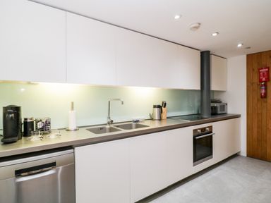 A kitchen with white cabinets steel countertop double sink oven dishwasher and coffee machine at Clarence Riverside Royal William Yard in Plymouth