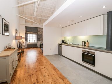 A modern kitchen and living space with white cabinets wooden floor and exposed ceiling at Clarence Riverside Royal William Yard in Plymouth