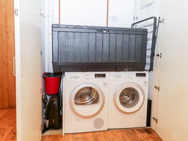 A laundry area with a washing machine and dryer side by side a black storage box on top and a red vacuum cleaner in a closet at Clarence Riverside Royal William Yard in Plymouth