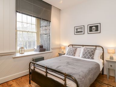 A bedroom with a metal bed frame gray bedding bedside tables with lamps and a window with gray blinds at Clarence Riverside Royal William Yard in Plymouth