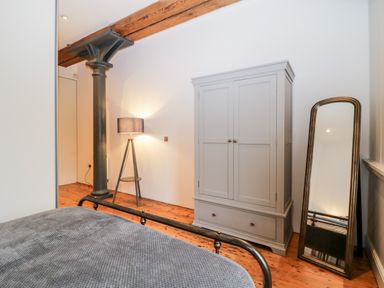A bedroom with a bed a grey wardrobe a floor lamp a standing mirror and a metal column at Clarence Riverside Royal William Yard in Plymouth