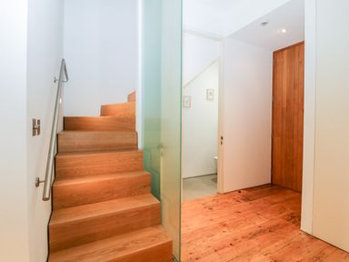 A wooden staircase with a metal handrail next to a hallway with wooden floor and partially open white door at Clarence Riverside Royal William Yard in Plymouth
