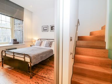 A bedroom with a metal bed and folded towels on the windowsill next to wooden stairs at Clarence Riverside Royal William Yard in Plymouth