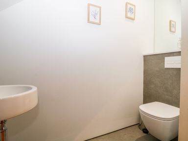 A small bathroom with a wall-mounted toilet and a wall-mounted sink with framed art on the wall at Clarence Riverside Royal William Yard in Plymouth