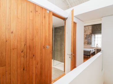 A hallway with a wooden wall door leading to a bathroom and a bedroom with a metal bed frame visible at Clarence Riverside Royal William Yard Plymouth
