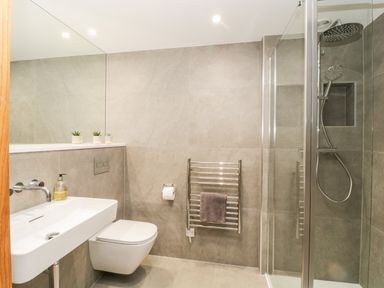 A bathroom with a wall mounted sink toilet towel rack and a shower enclosed by glass at Clarence Riverside Royal William Yard in Plymouth