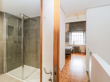 A hallway with wooden floor leading to a bedroom and a bathroom with glass shower enclosure at Clarence Riverside Royal William Yard in Plymouth