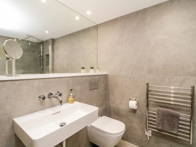 A bathroom with a wall-mounted sink toilet towel heater and shower behind glass at Clarence Riverside Royal William Yard in Plymouth