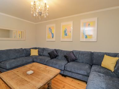 A living room with a large blue sectional sofa and wooden coffee table with a chandelier above at White Roses in Whitchurch near Monmouth