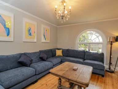 A living room with a blue sectional sofa wooden coffee table chandelier and arched window at White Roses in Whitchurch near Monmouth