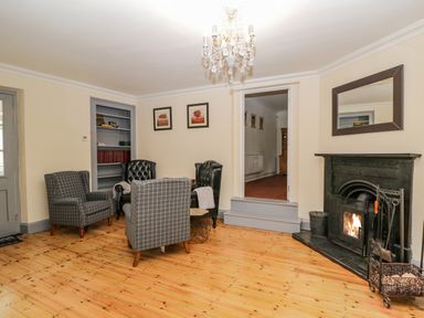 A sitting room with four armchairs a fireplace a chandelier and framed pictures at White Roses in Whitchurch near Monmouth