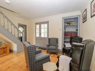 A sitting area with four chairs a wooden floor stairs and a bookshelf at White Roses in Whitchurch near Monmouth