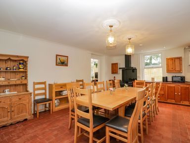 A dining room with a wooden table and chairs next to wooden cabinets and kitchen appliances at White Roses in Whitchurch near Monmouth