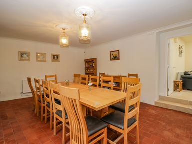 A dining room with a long wooden table and wooden chairs with black seats at White Roses in Whitchurch near Monmouth