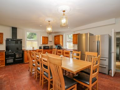A kitchen with a long wooden dining table and chairs two large refrigerators and wooden cabinets at White Roses in Whitchurch near Monmouth