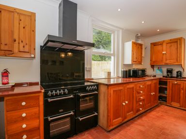 A kitchen with wooden cabinets a black stove and oven a window and countertop appliances at White Roses in Whitchurch near Monmouth