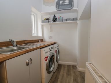 A utility room with a sink washing machine dryer shelving with laundry baskets at White Roses in Whitchurch near Monmouth