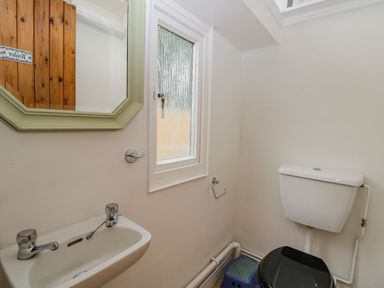 A toilet with a black seat a small sink a window and a mirror in a bathroom at White Roses in Whitchurch near Monmouth