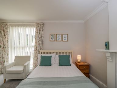 A bedroom with a bed with green pillows a white armchair a wooden nightstand with lamp and three botanical prints on the wall at White Roses in Whitchurch near Monmouth