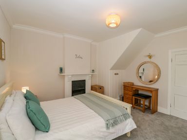 A bedroom with a bed, wooden dressing table, round mirror, and fireplace at White Roses in Whitchurch near Monmouth