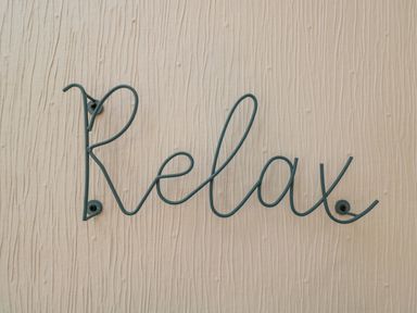 A metal wire sculpture spelling the word relax mounted on a textured beige wall at White Roses in Whitchurch near Monmouth