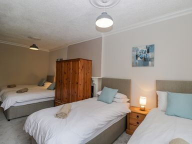 A bedroom with three single beds pillows and rolled towels a wooden wardrobe and nightstand with a lamp and painting at White Roses in Whitchurch near Monmouth