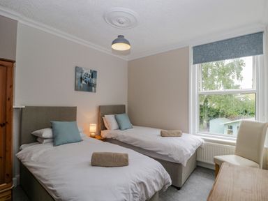 A bedroom with two single beds a wooden wardrobe a chair and a window at White Roses in Whitchurch near Monmouth