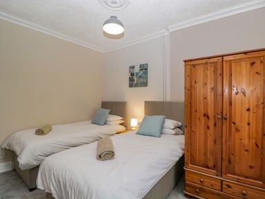 A bedroom with two single beds with rolled towels and cushions a wooden wardrobe and a small bedside lamp at White Roses in Whitchurch near Monmouth