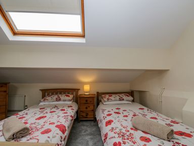 A bedroom with two single beds with floral bedding and rolled towels under a skylight at White Roses in Whitchurch near Monmouth