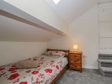 A bedroom with a single bed with floral bedding next to a wooden nightstand with a lamp and carpeted stairs at White Roses in Whitchurch near Monmouth