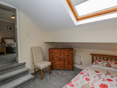 A bedroom with a bed a wooden dresser a beige chair and a skylight window at White Roses in Whitchurch near Monmouth