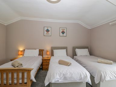 A bedroom with three single beds each with a white pillow and blanket and a folded towel on top with two side tables and lamps between the beds at White Roses Whitchurch near Monmouth
