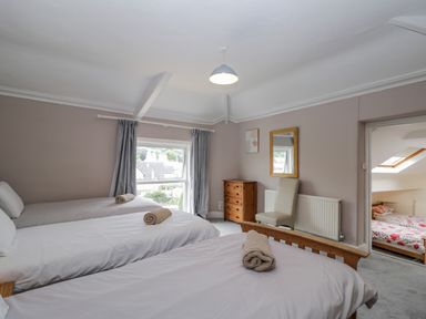 A bedroom with three single beds with rolled towels on each and a wooden dresser with a chair at White Roses in Whitchurch near Monmouth