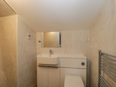 A small bathroom with a white sink, cabinet, toilet, mirror, and a metal towel rack at White Roses in Whitchurch near Monmouth