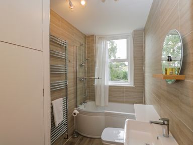 A bathroom with a bathtub shower combo a towel rack toilet sink and a round mirror at White Roses in Whitchurch near Monmouth