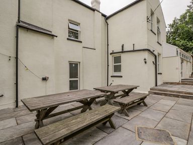 An outdoor patio area with two wooden picnic tables on a stone tiled floor at White Roses in Whitchurch near Monmouth