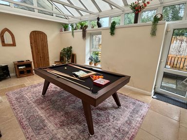 A billiards table in a room with a glass ceiling and plants on a shelf at White Roses in Whitchurch near Monmouth