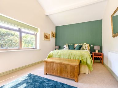 A bedroom with a green accent wall and bed with green bedding a wooden chest at the foot and a blue rug on the floor at The Paddock in Honington near Shipston-On-Stour