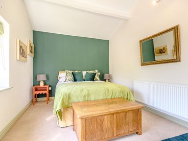 A bedroom with a bed and green bedding a wooden chest and a mirror on the wall at The Paddock in Honington near Shipston-On-Stour