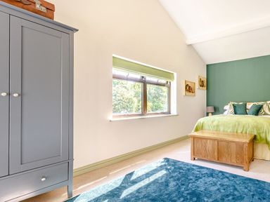 A bedroom with a blue wardrobe a wooden chest at the foot of the bed and a window with a green blind at The Paddock in Honington near Shipston-On-Stour